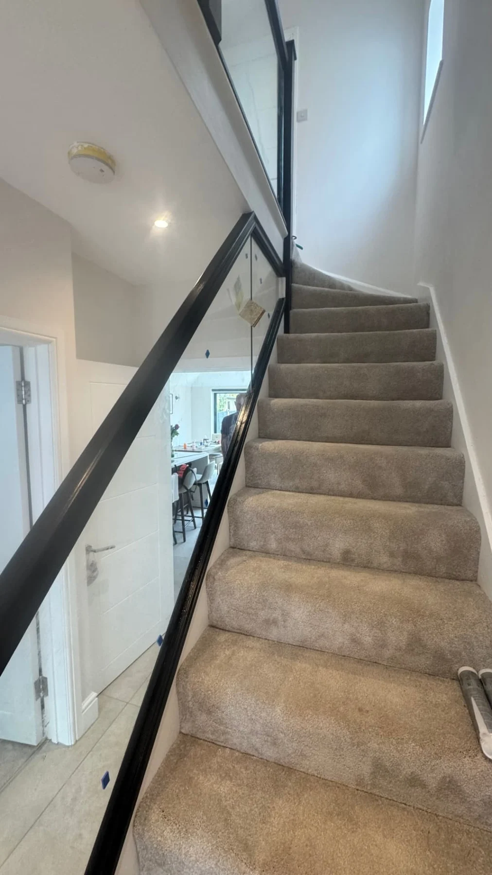 Carpeted staircase with a dark-framed glass balustrade