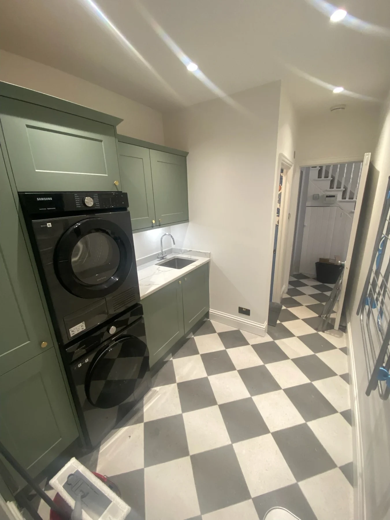 Green utility room with stacked laundry appliances and chequered floor