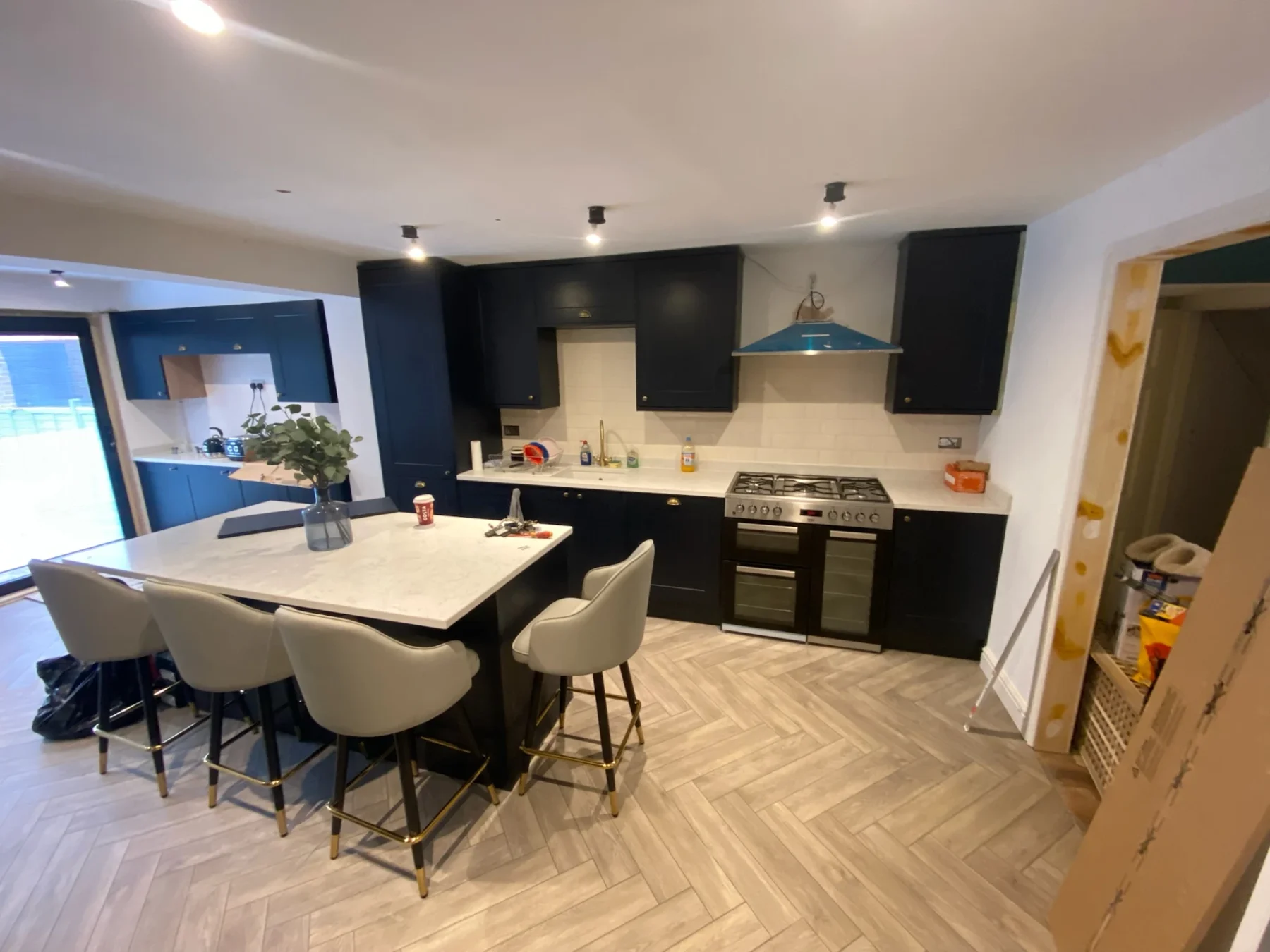 Dark fitted kitchen with island seating, range cooker and herringbone flooring