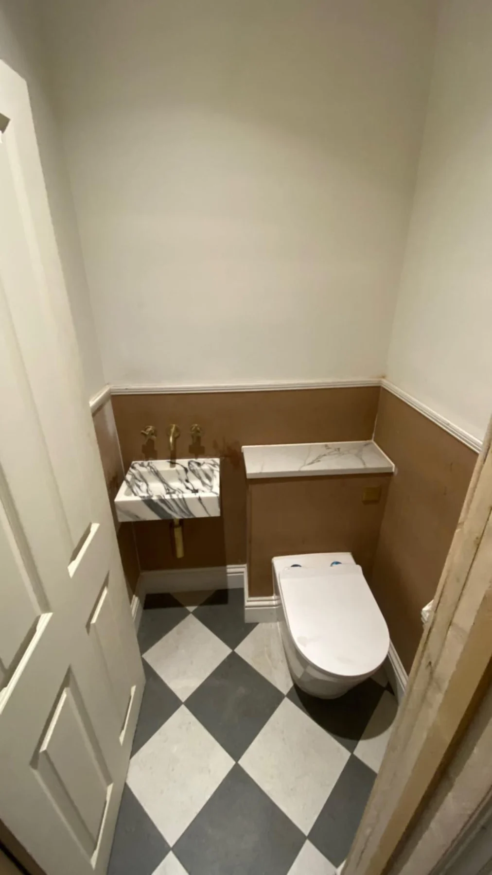 Cloakroom with white toilet, timber panelling and a black-and-white tiled floor