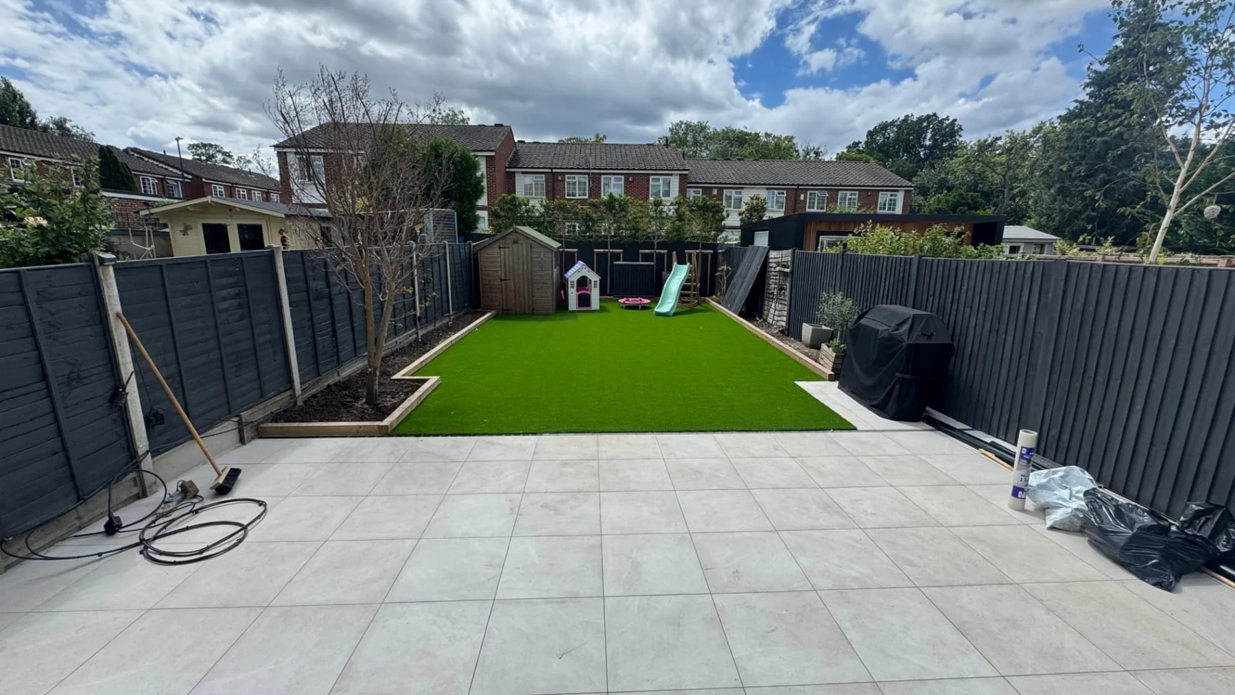 Garden landscaping with a paved patio, artificial lawn and dark fencing