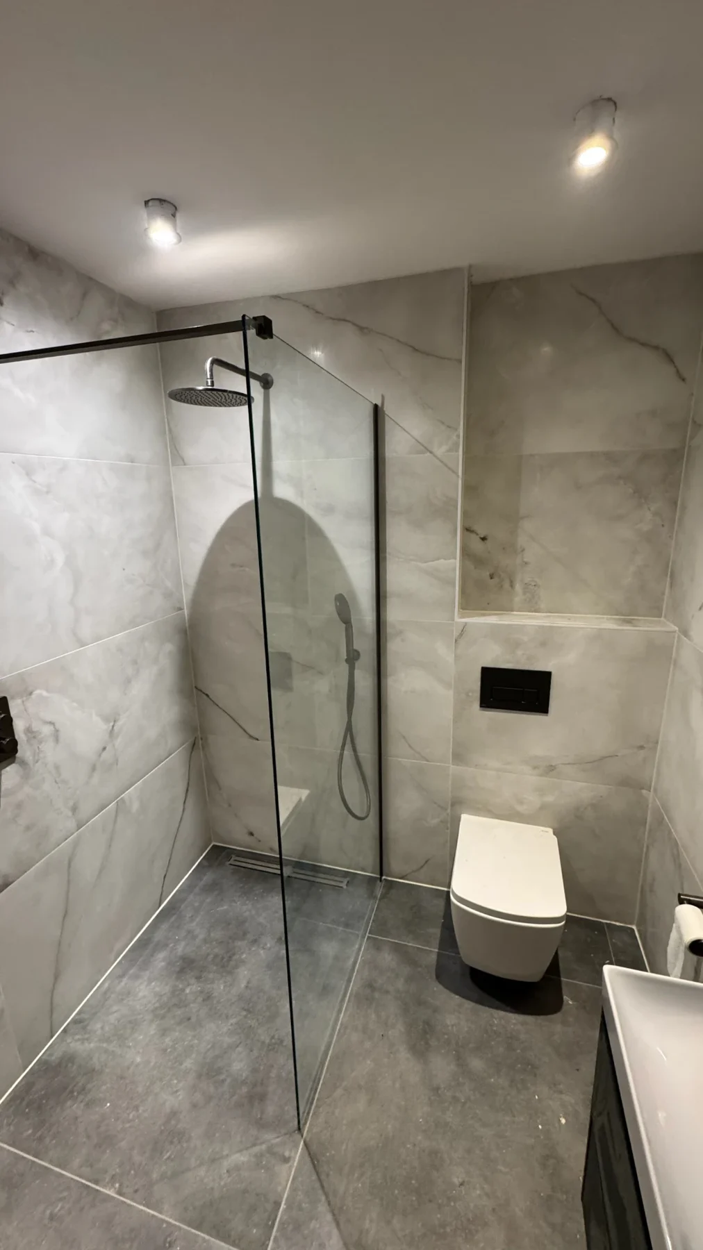 Stone-effect tiled bathroom with glass shower enclosure and wall-hung toilet